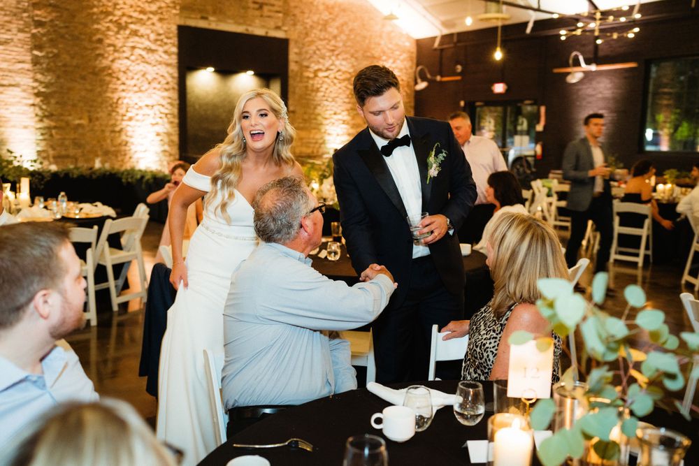 Guests celebrate with newlyweds at an intimate wedding reception in a rustic brick venue with warm lighting.