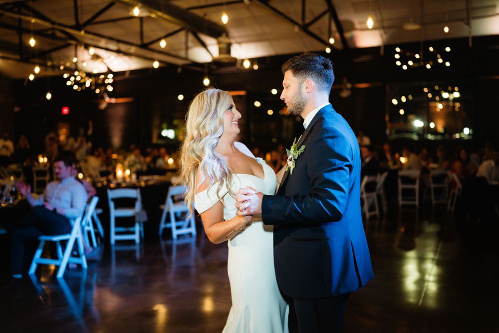 First dance moment at wedding reception with romantic lighting and white chairs in background.