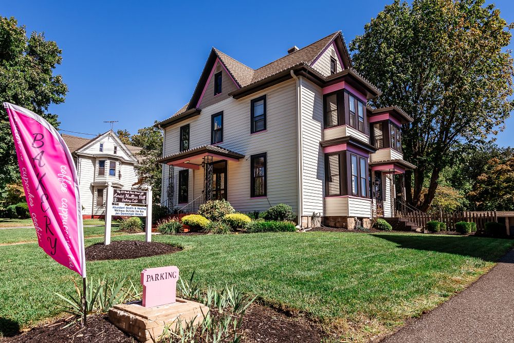 A beautiful Victorian-style house with pink trim and a manicured lawn on a sunny day.