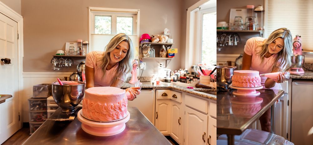 Baker working on decorating a pink cake in a sunlit kitchen with white cabinets.