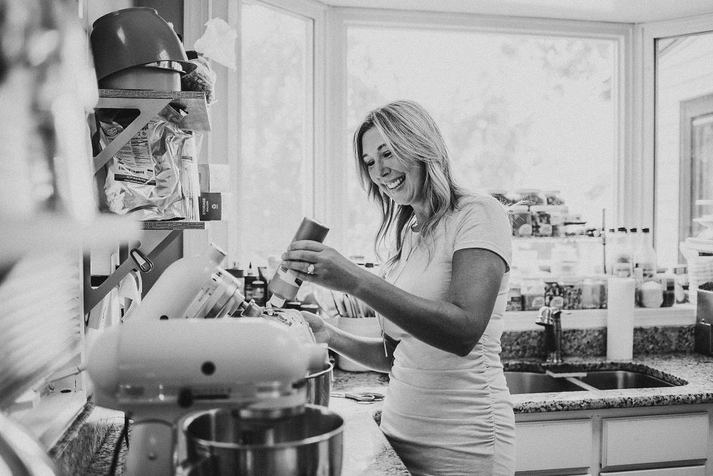 Black and white photo of baker using stand mixer in bright kitchen setting.