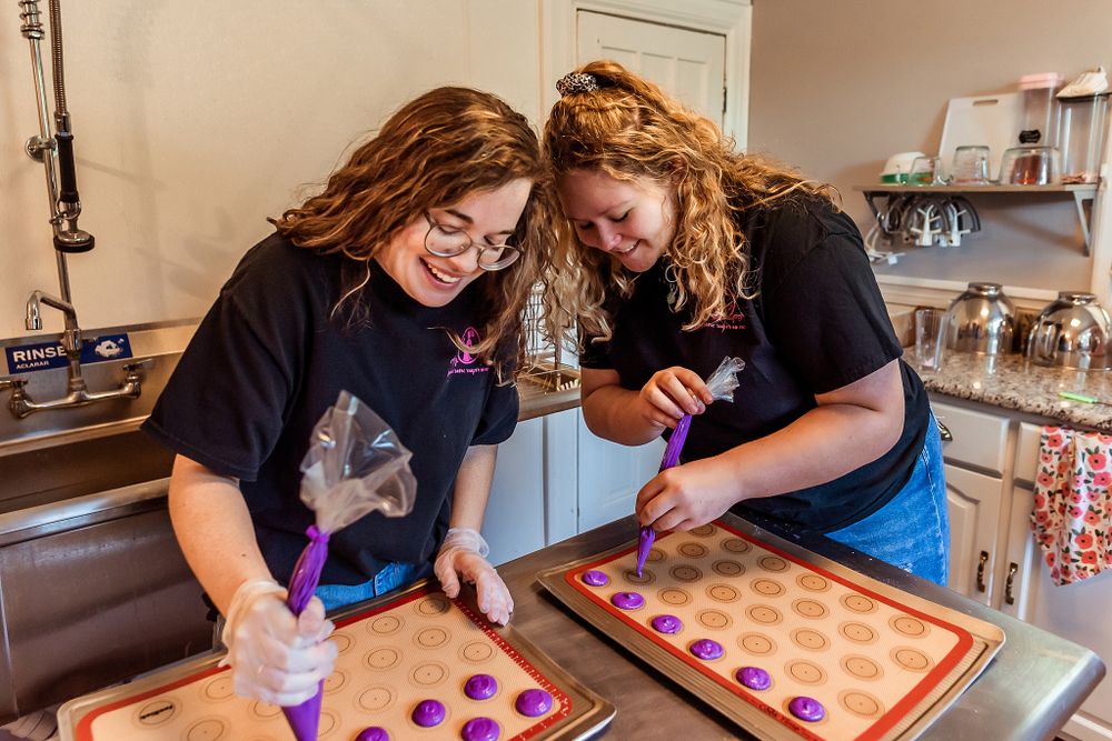 Bakers in aprons pipe decorative toppings onto baked goods in a commercial kitchen.
