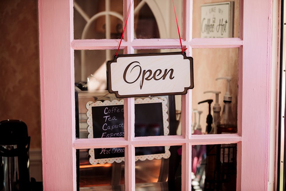 Open sign hanging in a pink-framed window of a bakery shop.