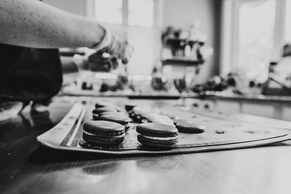 Black and white image of macarons being arranged on a baking sheet in a bakery setting.