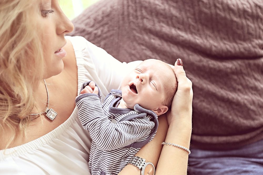 A loving mother gazes down at her yawning newborn baby cradled in her arms.