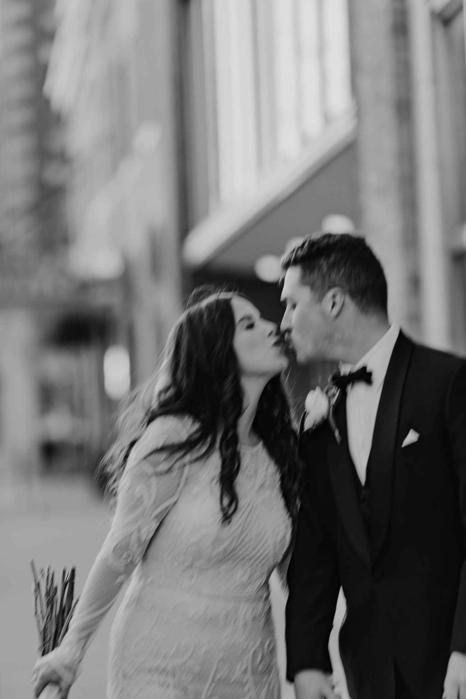 Romantic black and white wedding photo of a couple sharing a tender kiss in formal attire.