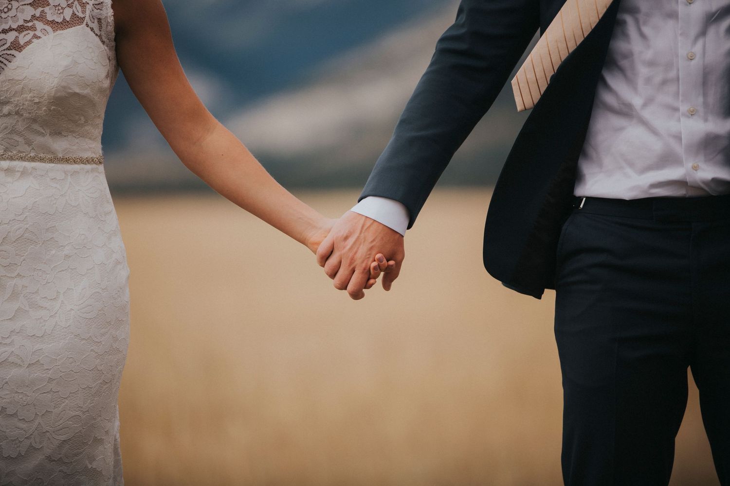 Close-up shots of couple holding hands with wedding attire details against natural backdrop.