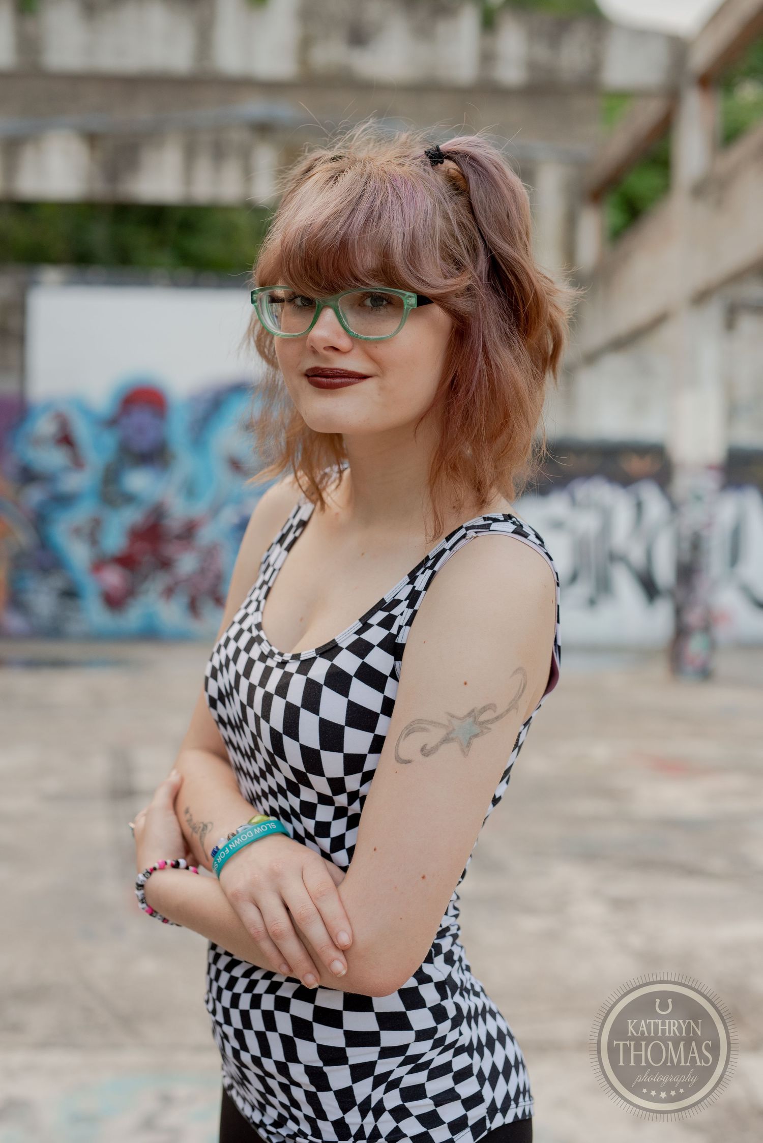 Fashion portrait featuring a black and white checkered top and glasses in an industrial setting with graffiti.