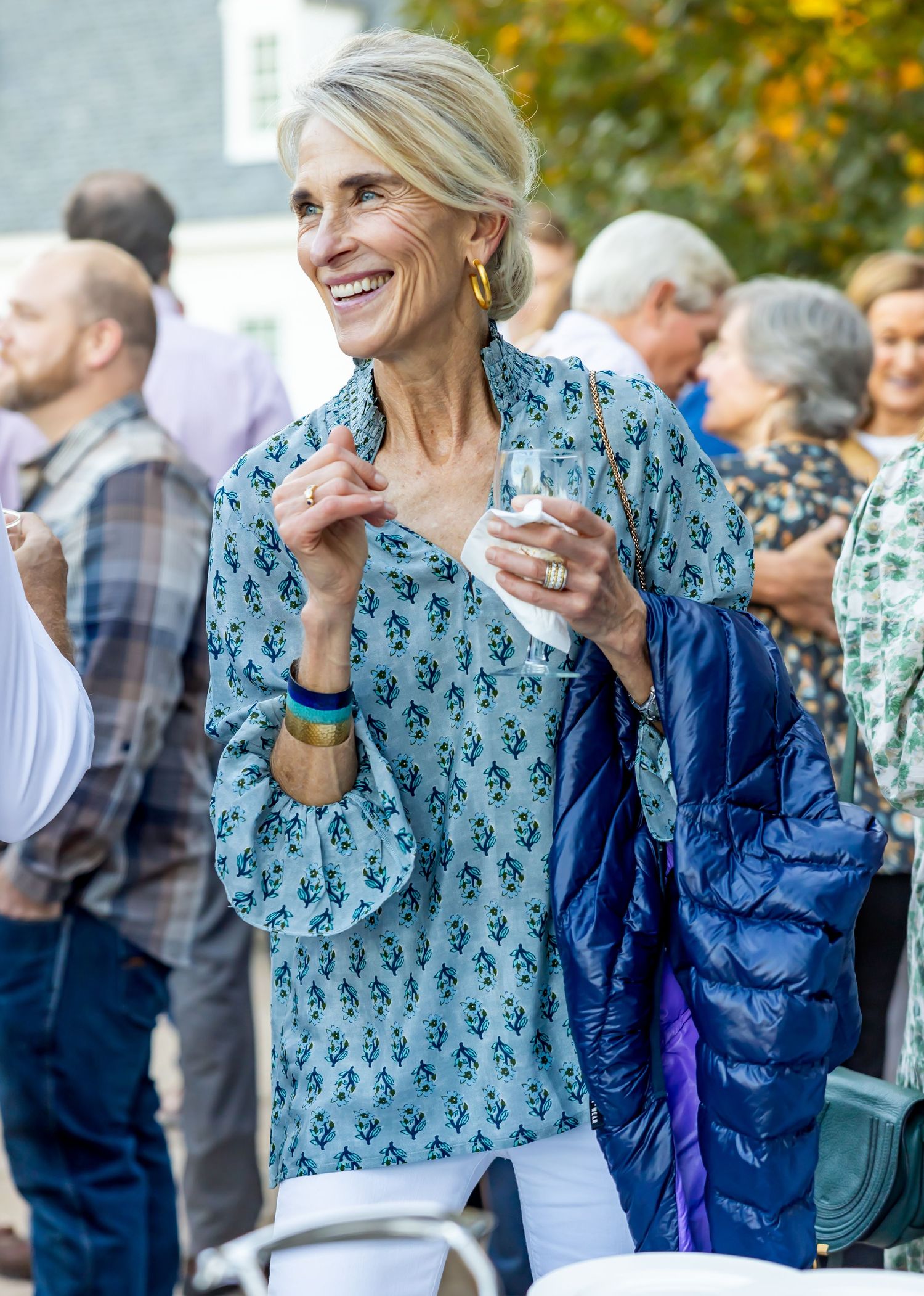 Elegant woman in patterned blue top enjoying outdoor social gathering.