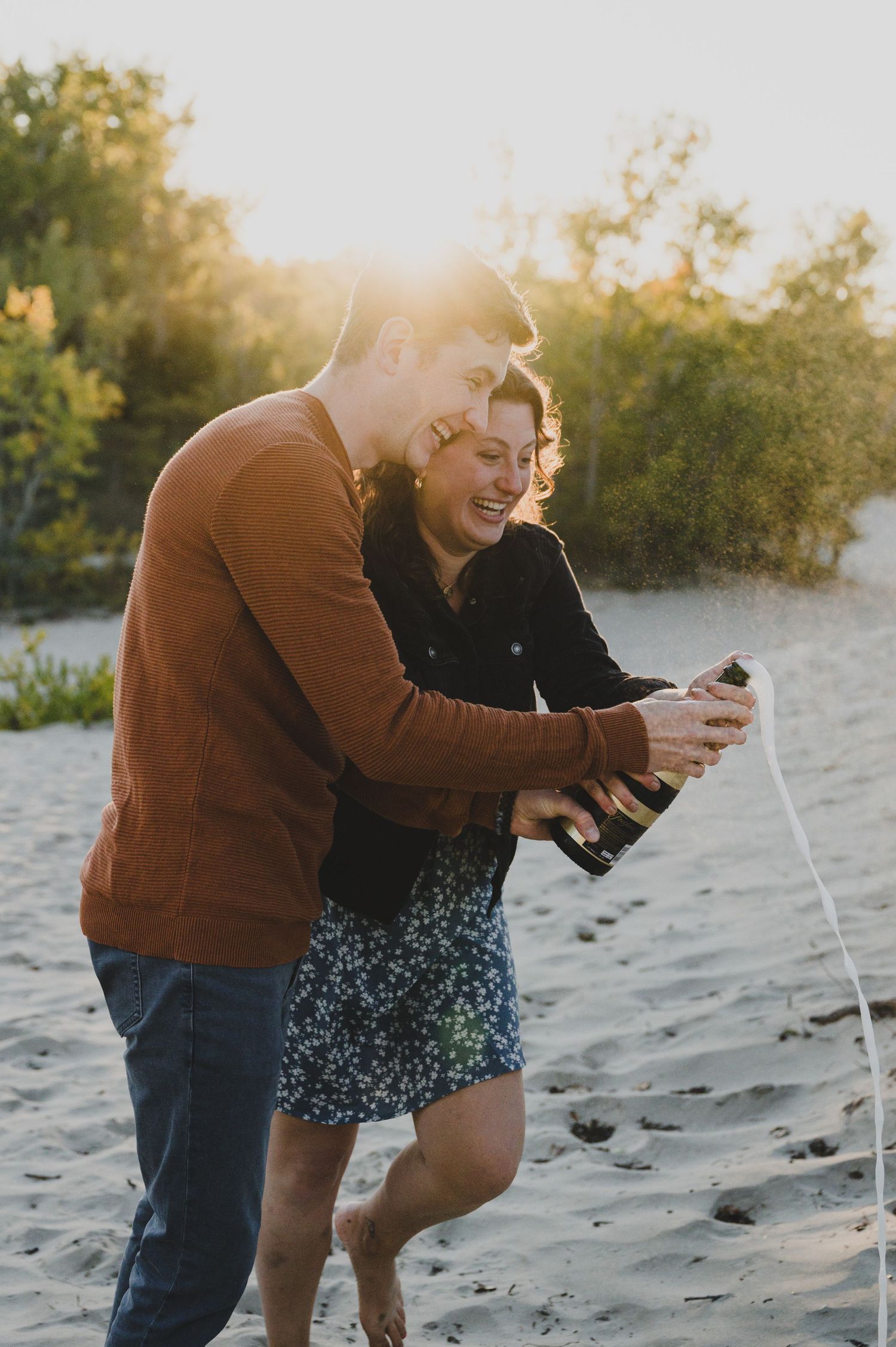 Couple laughing and playing together on a sandy beach at sunset.