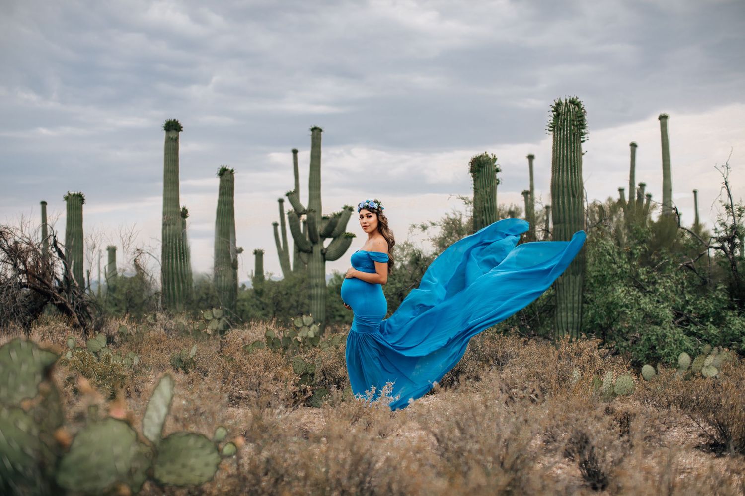 Tucson portrait of a woman twirling in a flowing blue dress in the desert surrounded by saguaros and cactus plants.