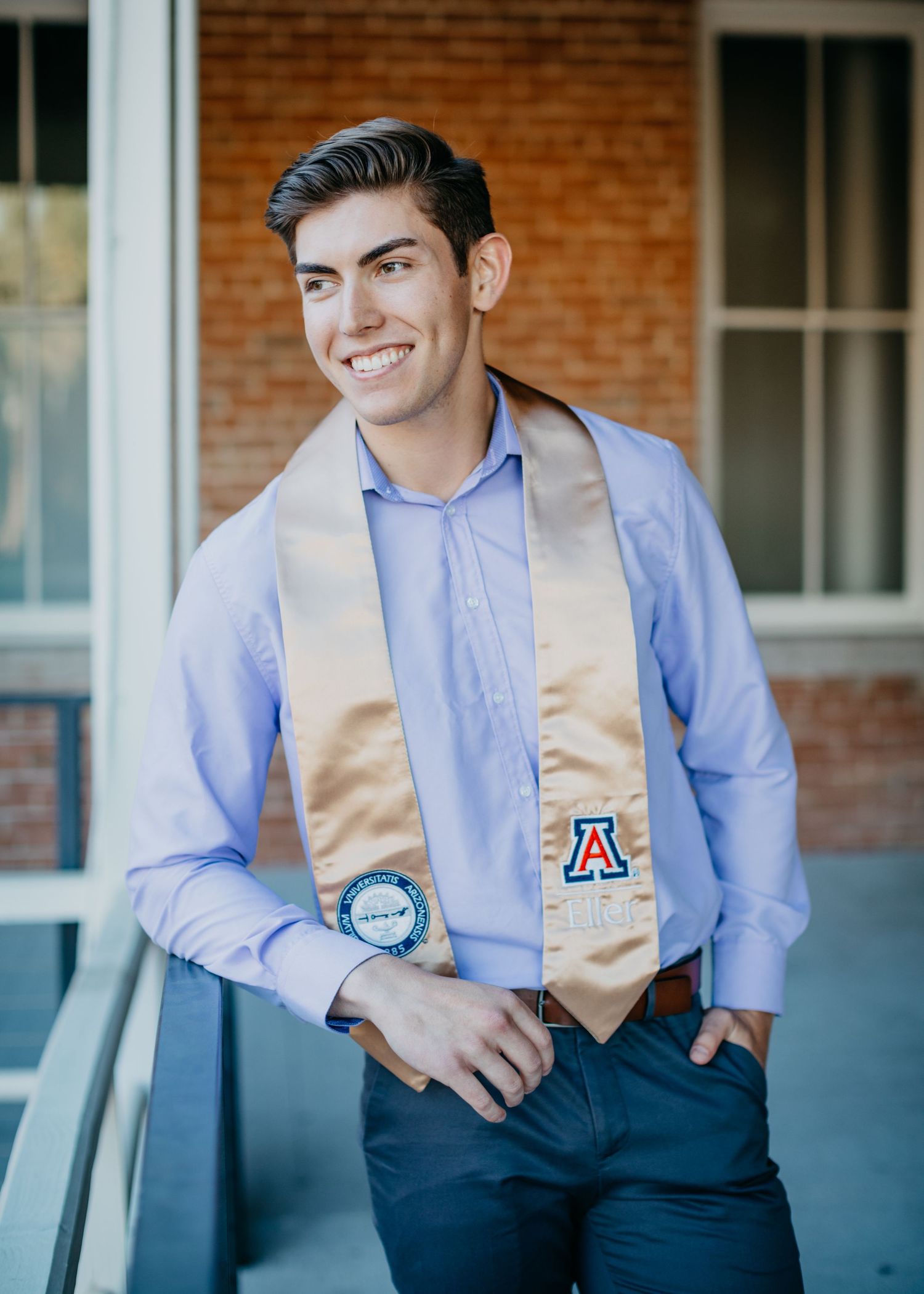 Tucson senior photo of a graduate leaning casually on a railing with his cap and stole in a modern outdoor setting.
