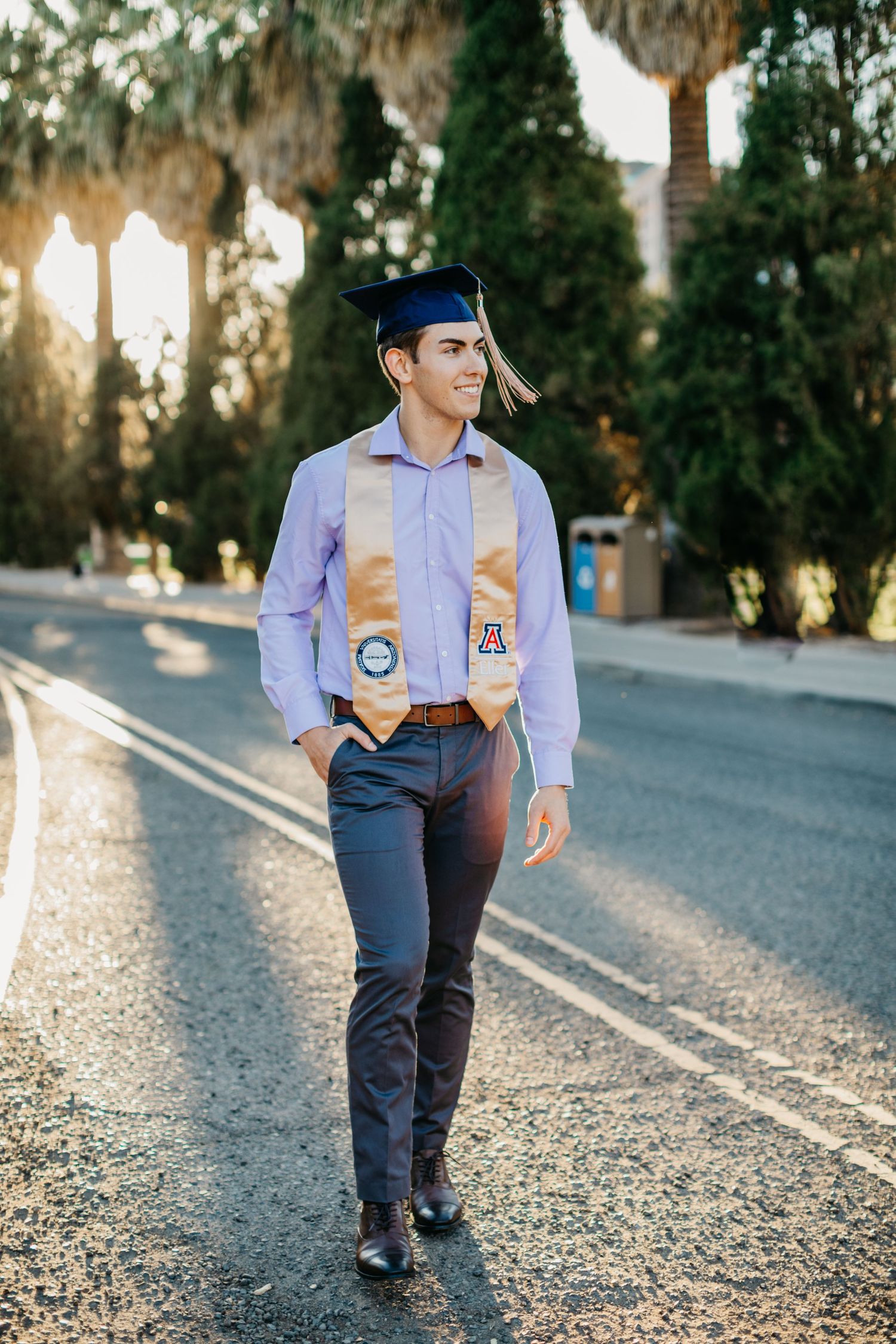 Tucson senior portrait of a young man walking confidently outdoors at golden hour wearing his graduation stole.
