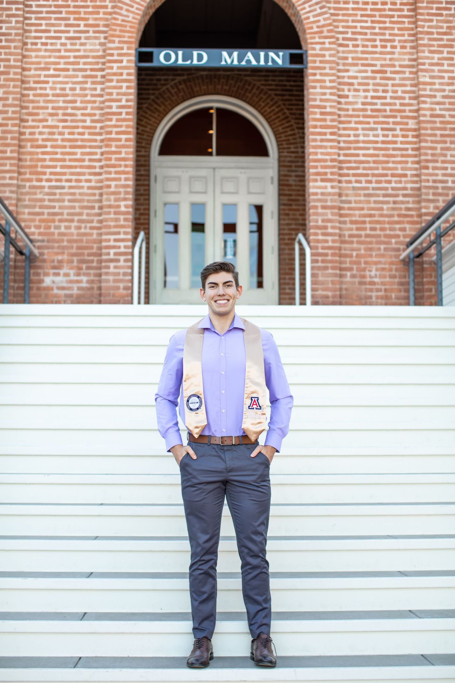 Tucson senior portrait of a graduate standing proudly on university steps wearing his stole and dress shirt.