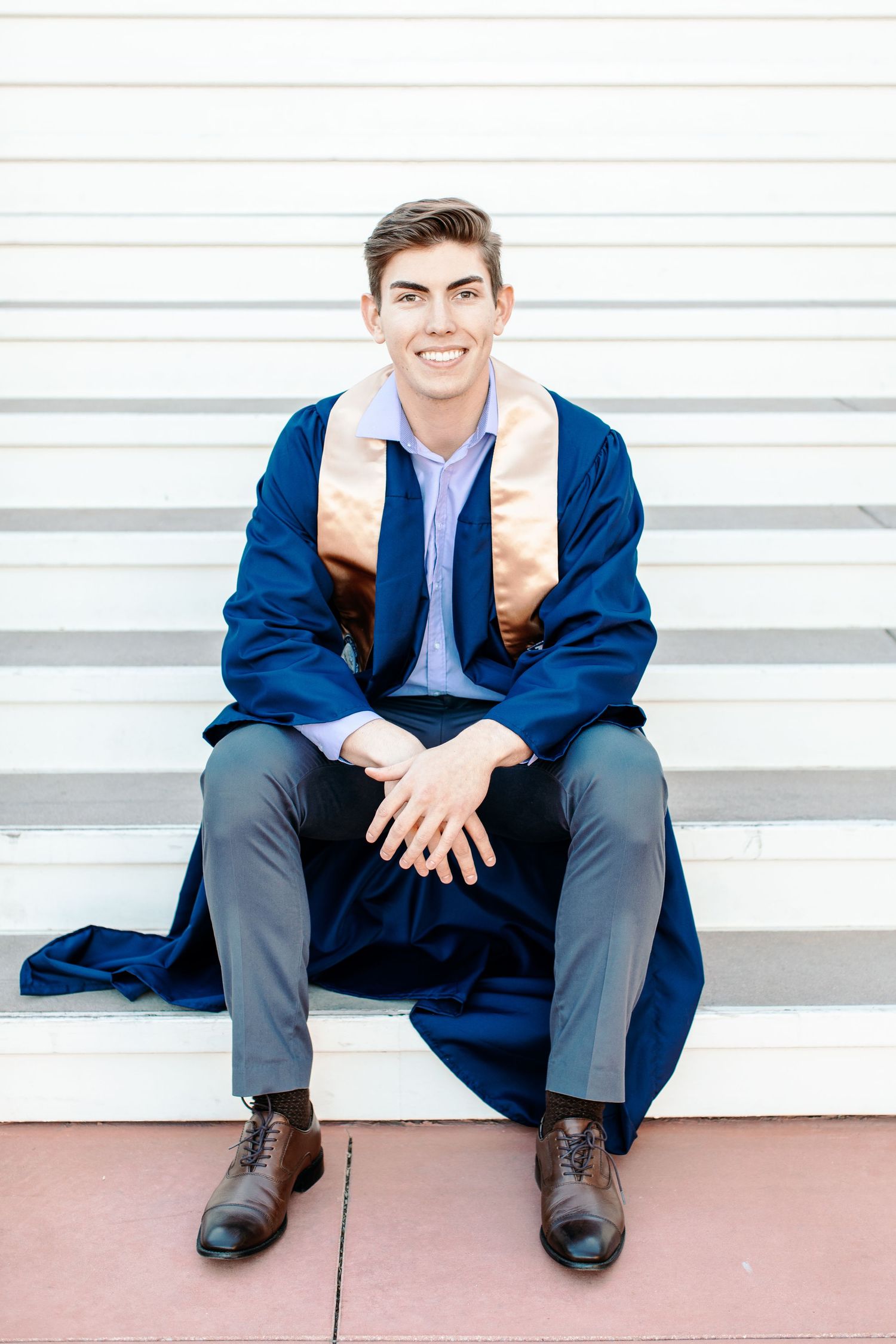 Tucson senior graduation portrait of a young man sitting on steps wearing his cap, gown, and stole.