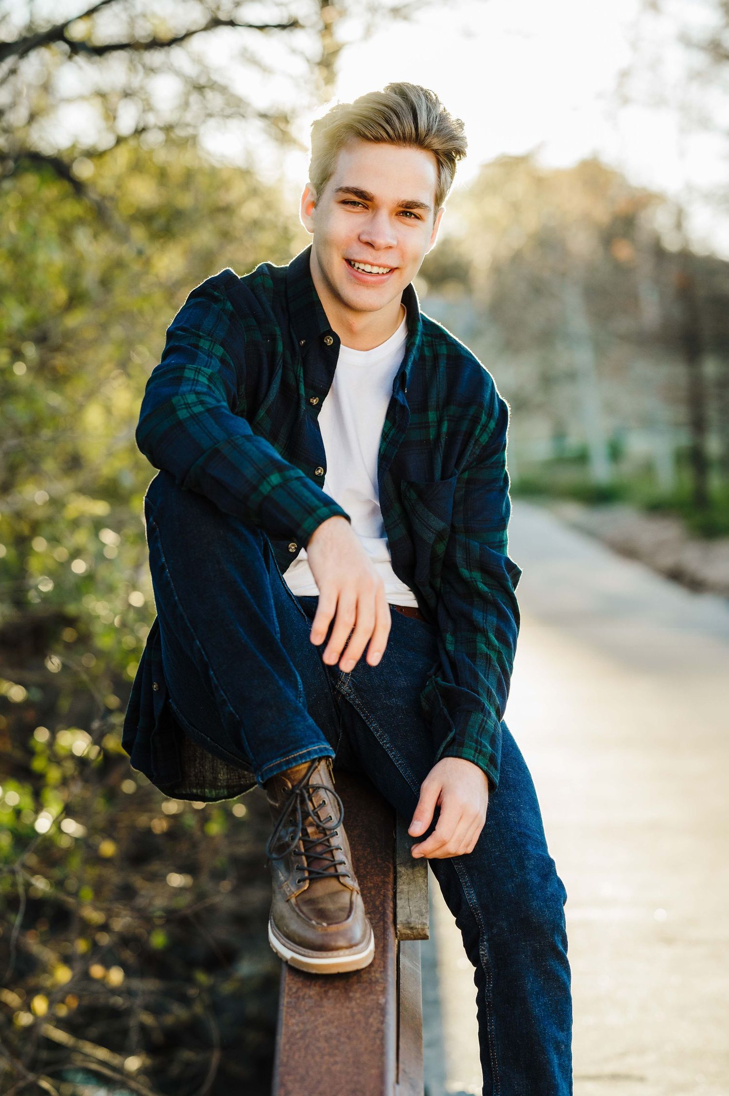 Stylish person in plaid jacket sits outdoors during golden hour portrait session.