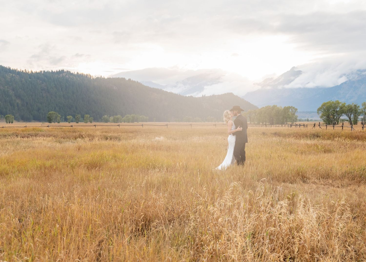 A romantic moment captured in a golden meadow with misty mountains and sunlight in the background.