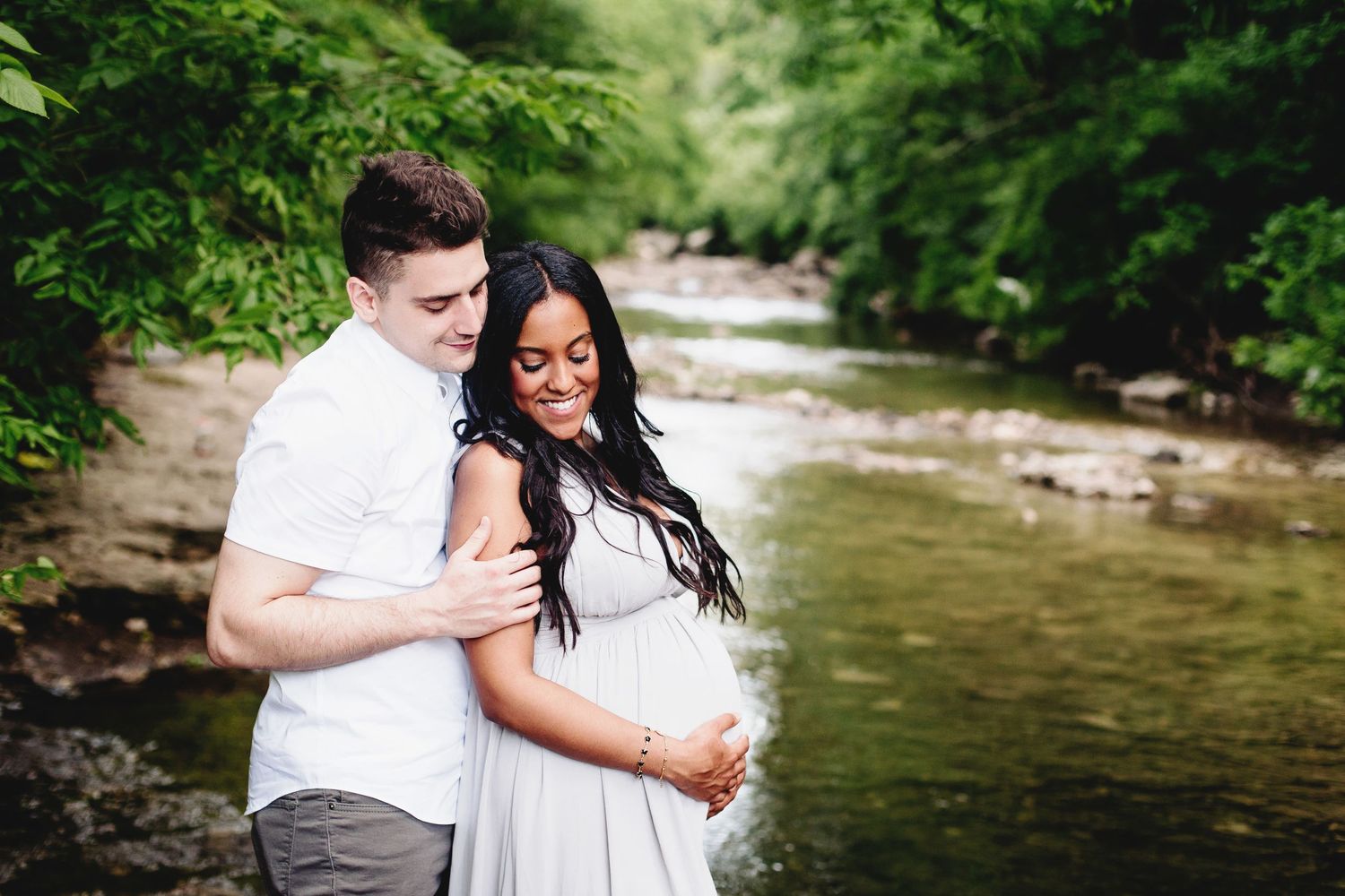 couple smiling for maternity photos near small river