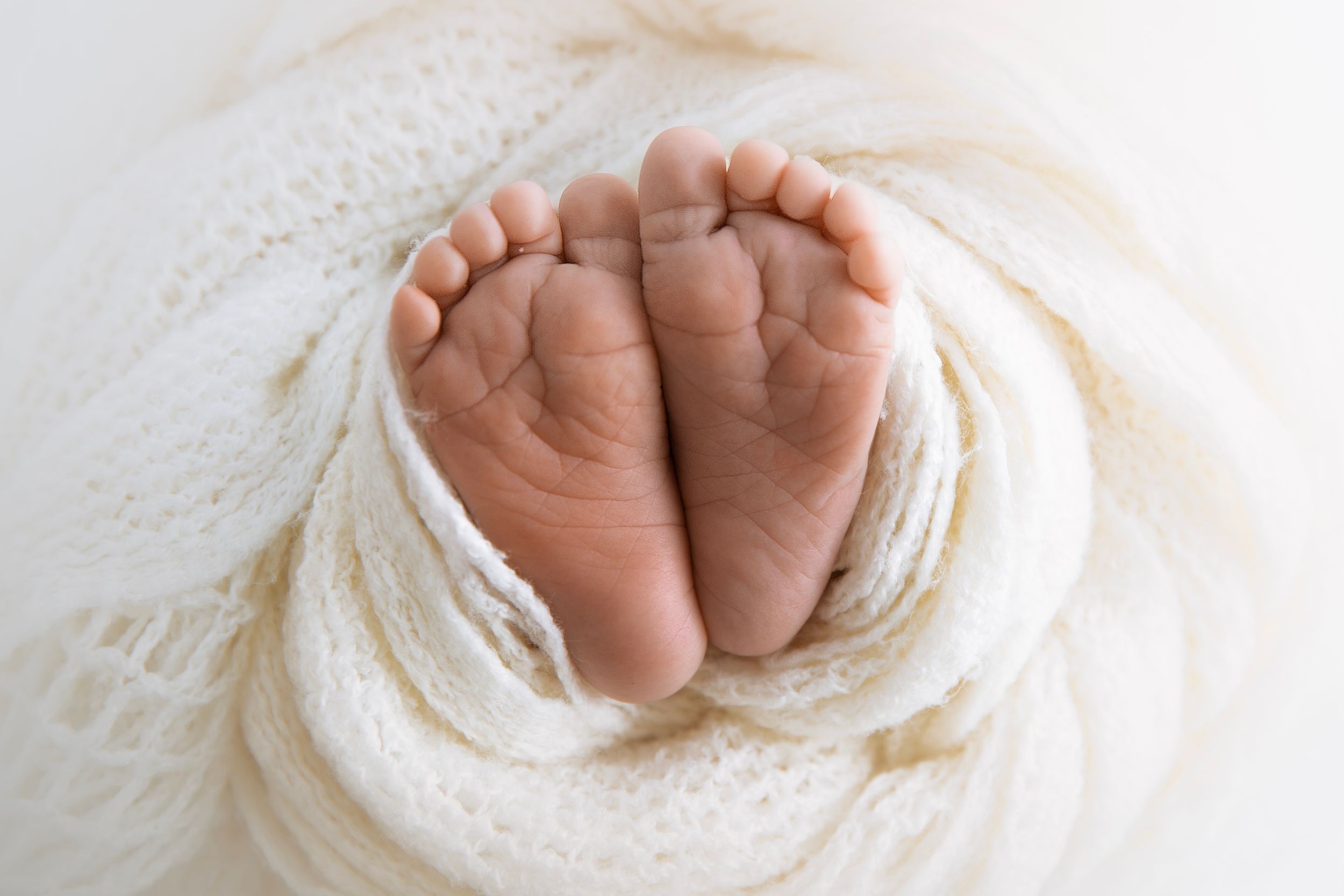Close-up of tiny newborn feet nestled in white textured fabric.
