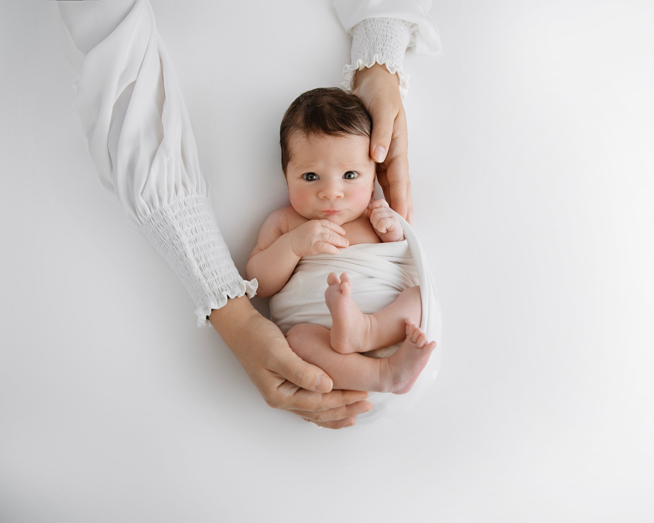Overhead view of newborn in white setting showing gentle parental touch.