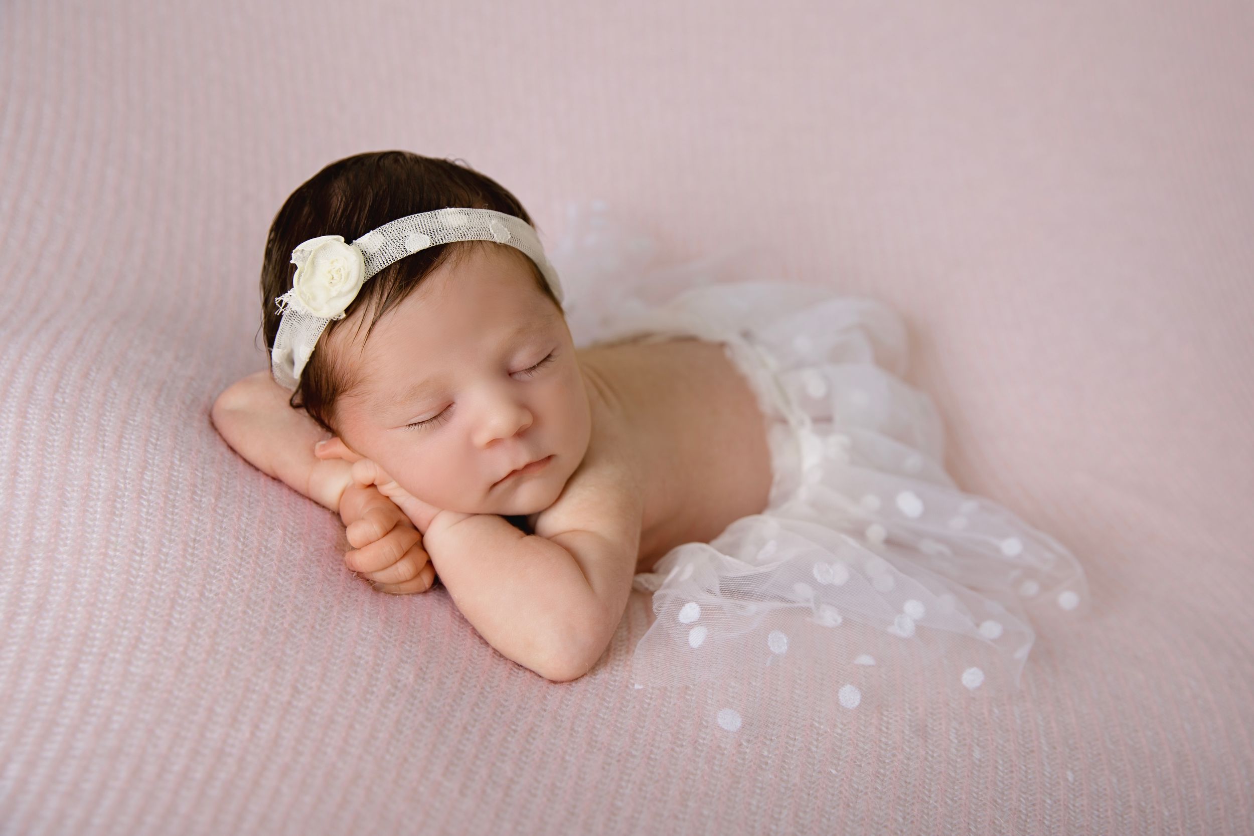 Artistic newborn photography series with baby on pink textured backdrop wearing white accessories.