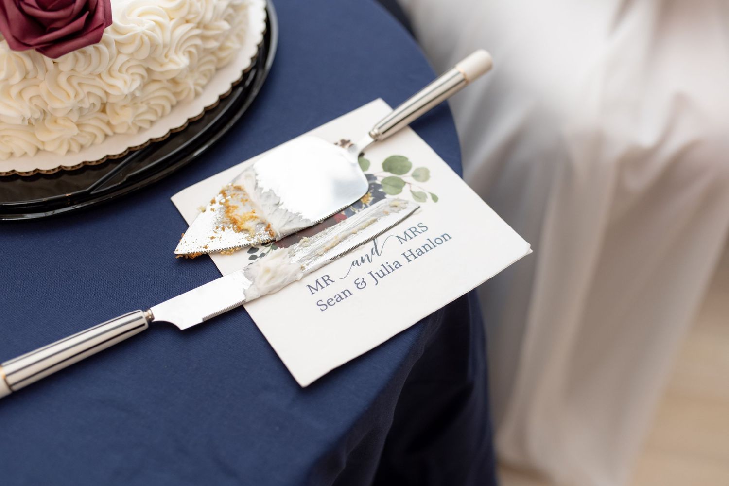 Wedding cake serving set with floral name card on navy blue tablecloth.