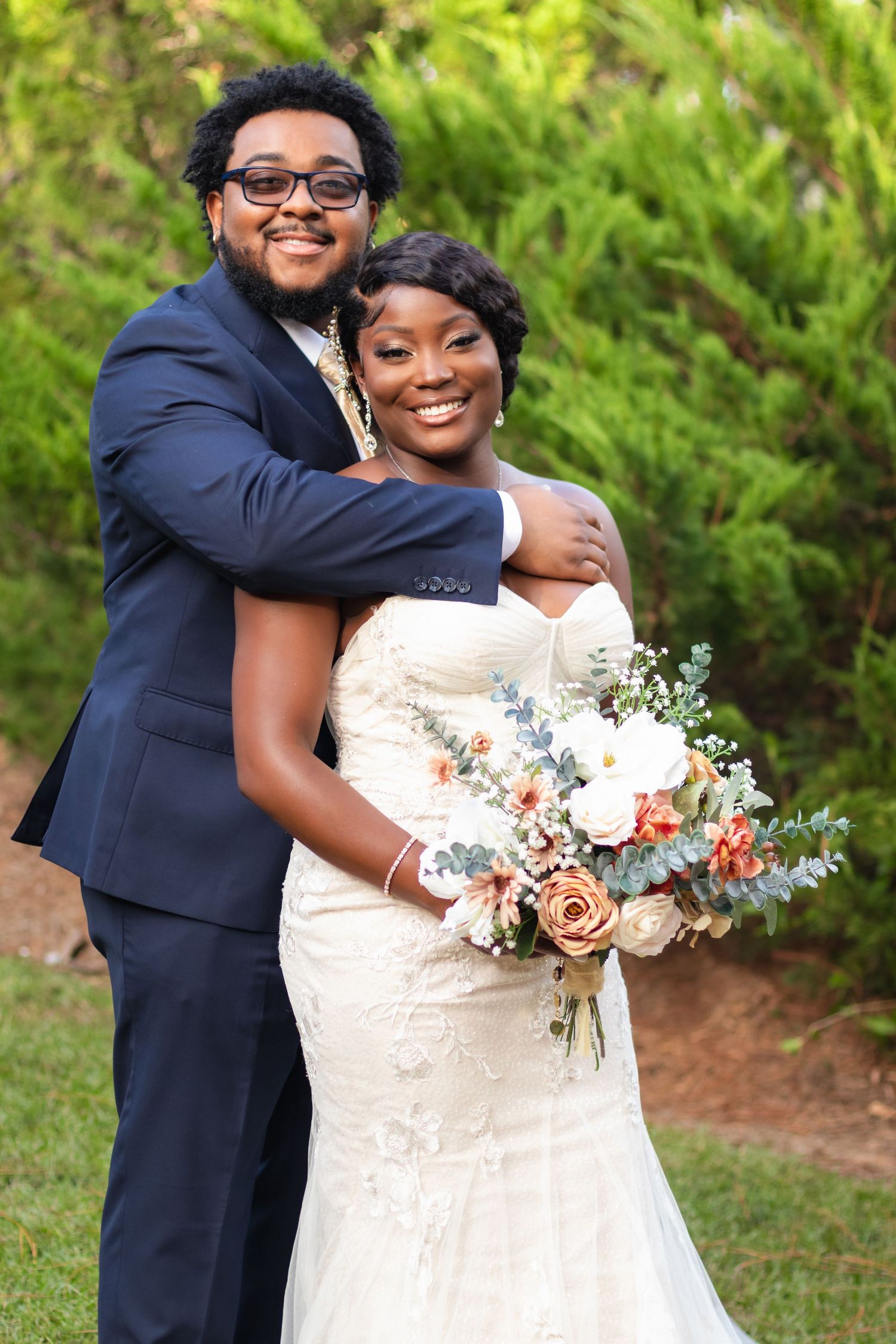 Wedding couple embraces while holding a beautiful pastel floral bouquet outdoors.