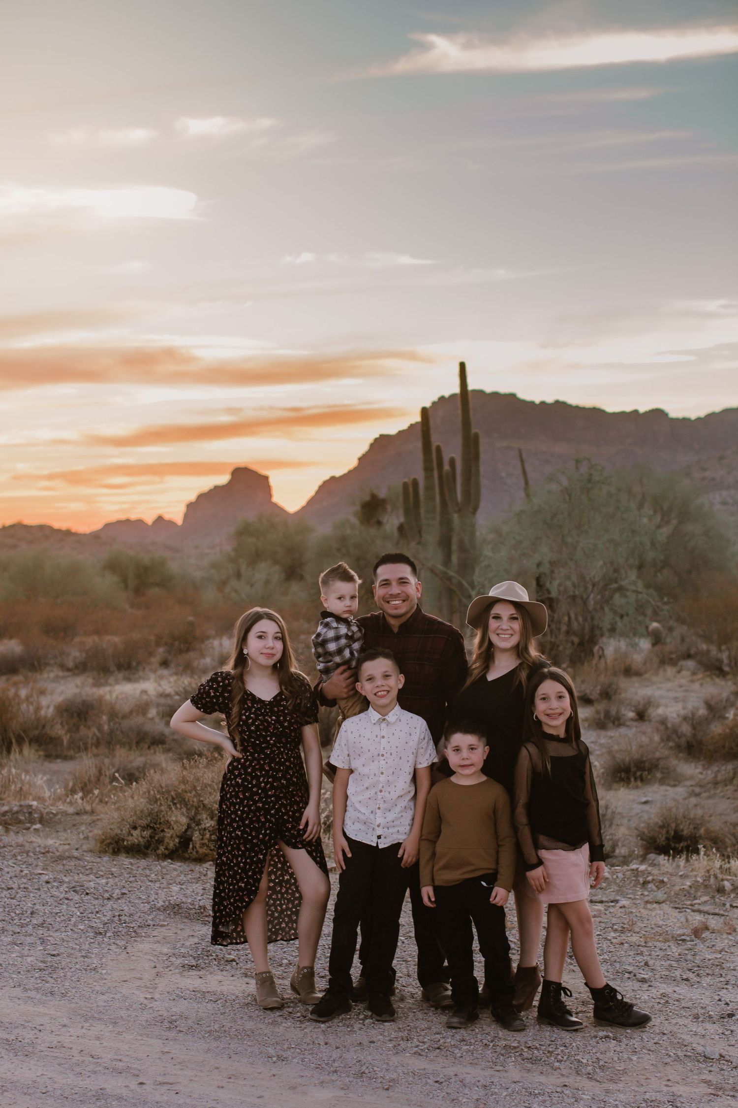 A group sits together on desert terrain with saguaro cacti and mountains silhouetted against a golden sunset sky.