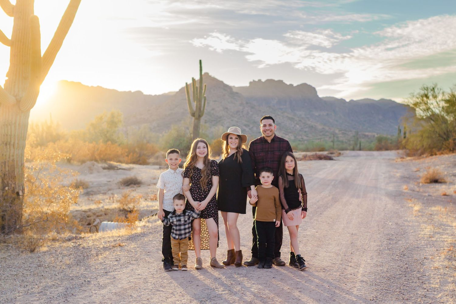 Family portrait in desert landscape with mountains and saguaro cactus at sunset.