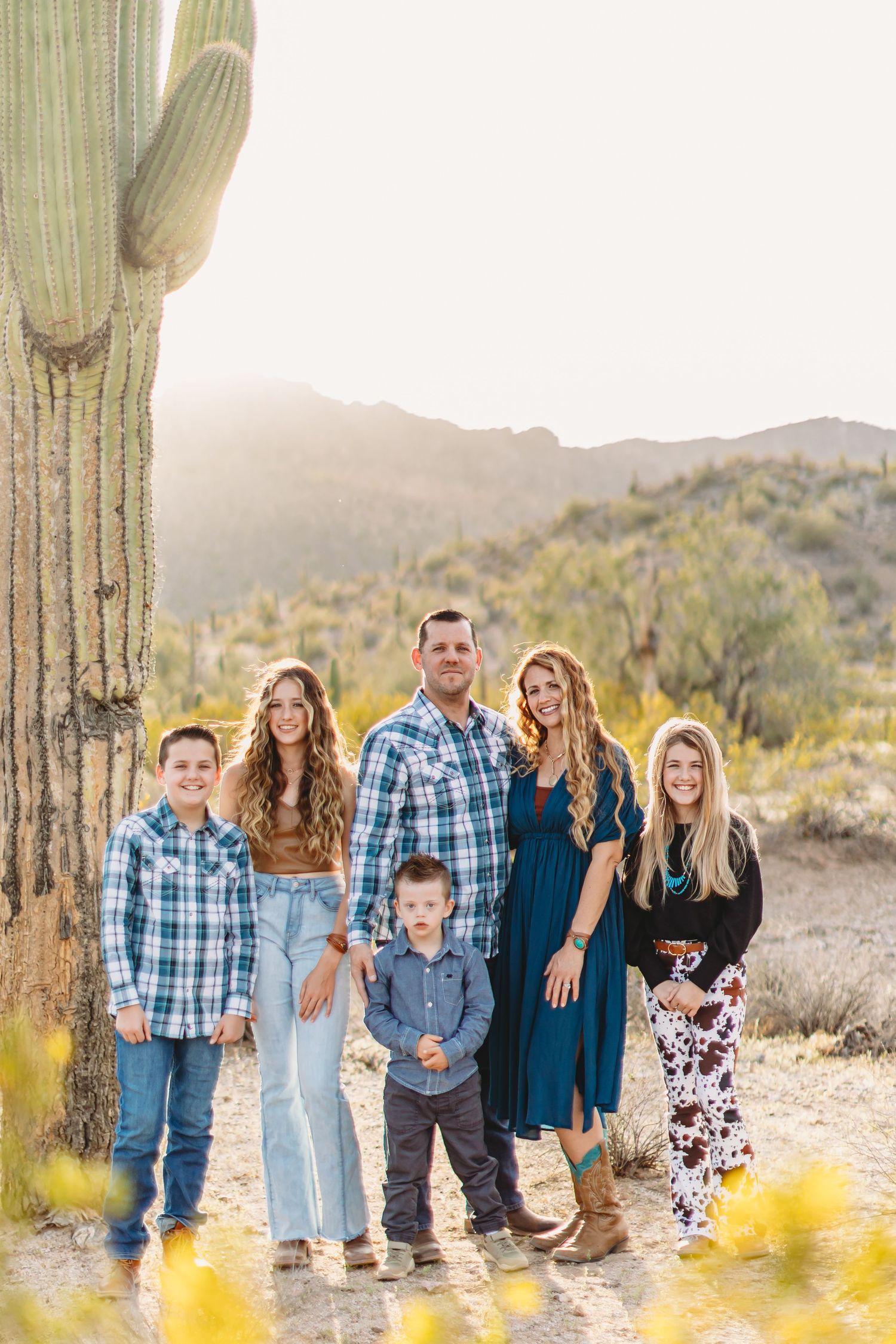 Family poses together in front of a large saguaro cactus in the Arizona desert at sunset.