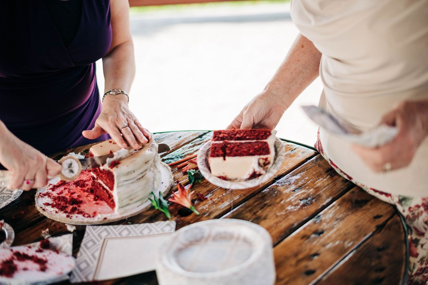 women cutting and serving red velvet wedding cake