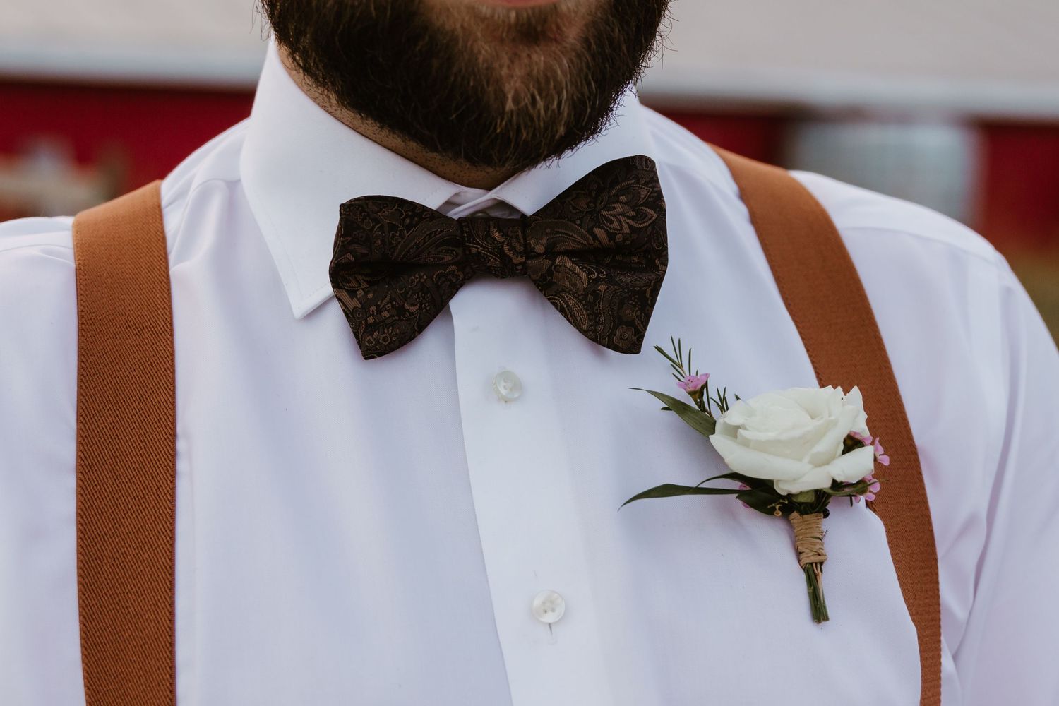 Groom's attire detail showing brown bow tie, white shirt, suspenders and white rose boutonniere.