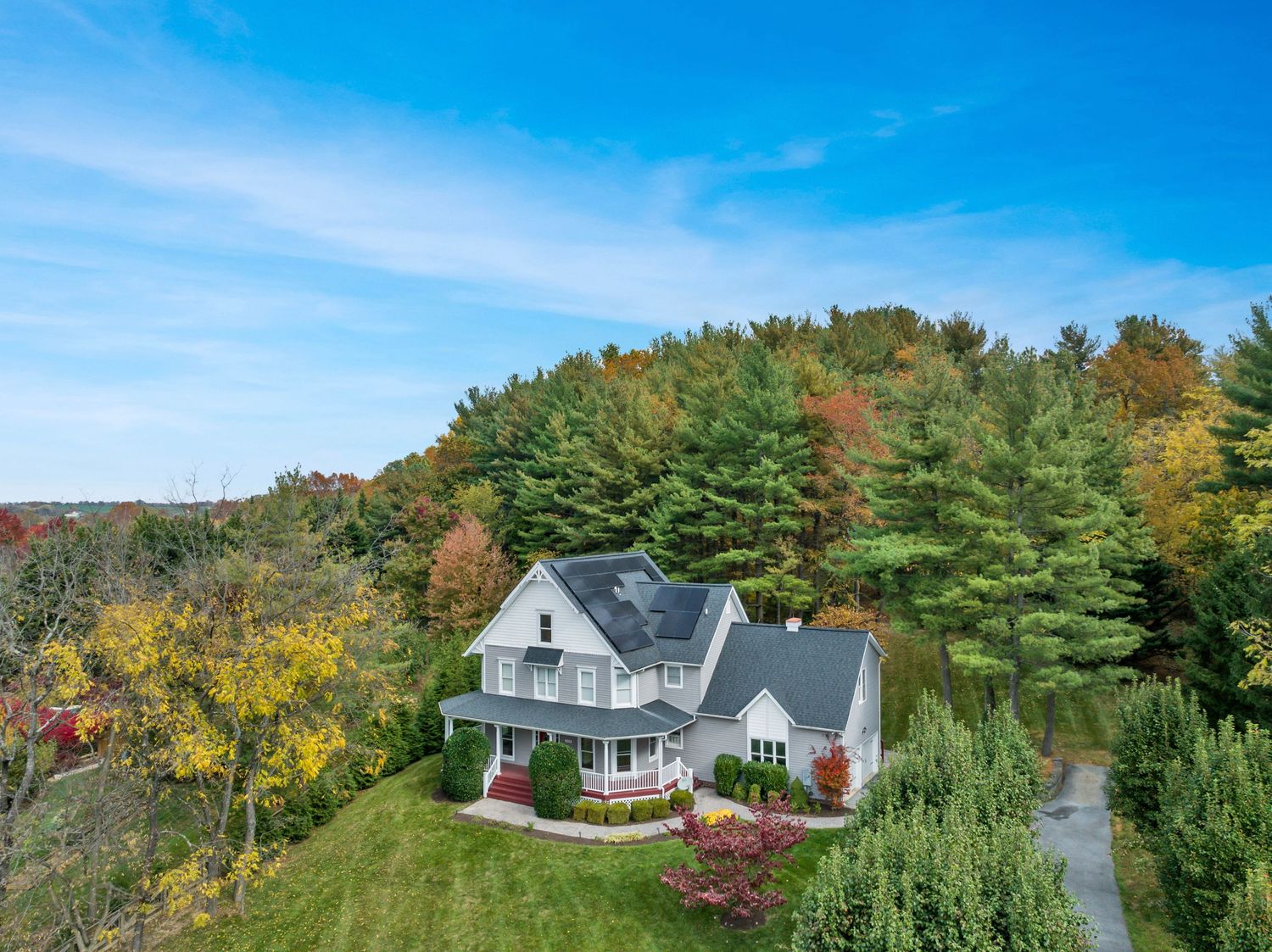 Aerial view of a white Victorian-style house nestled among fall foliage on a hillside.