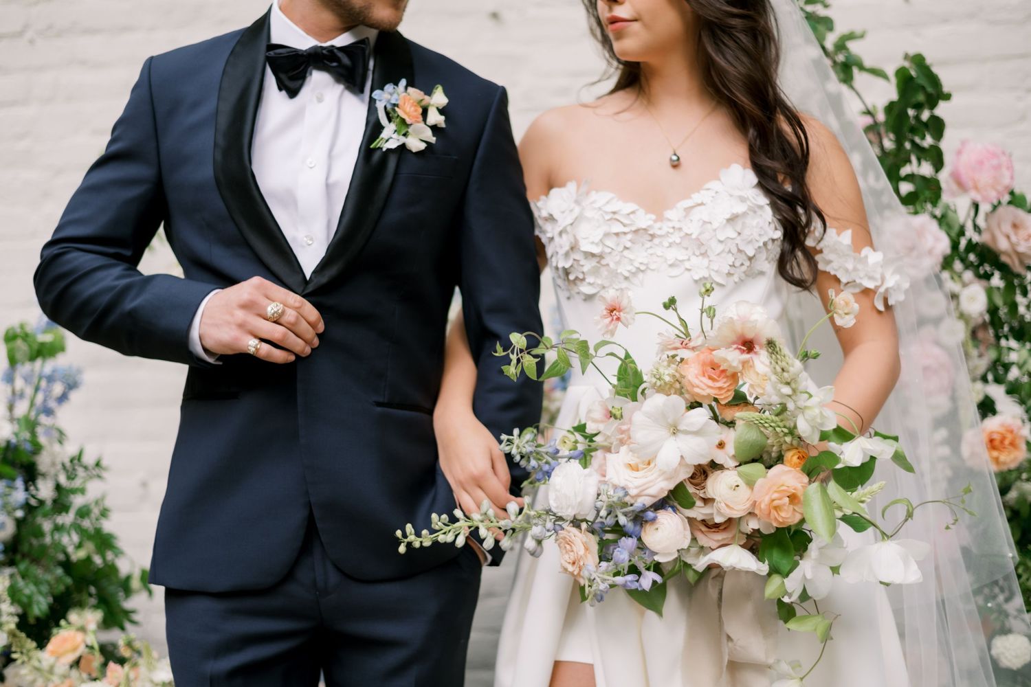 Wedding couple detail shot showing black tuxedo and white dress with peach floral bouquet.