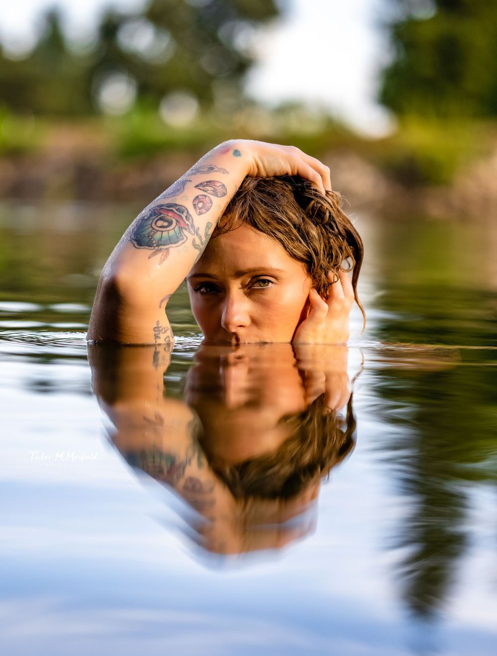 Artistic reflection portrait in calm water showing tattoo on submerged subject.