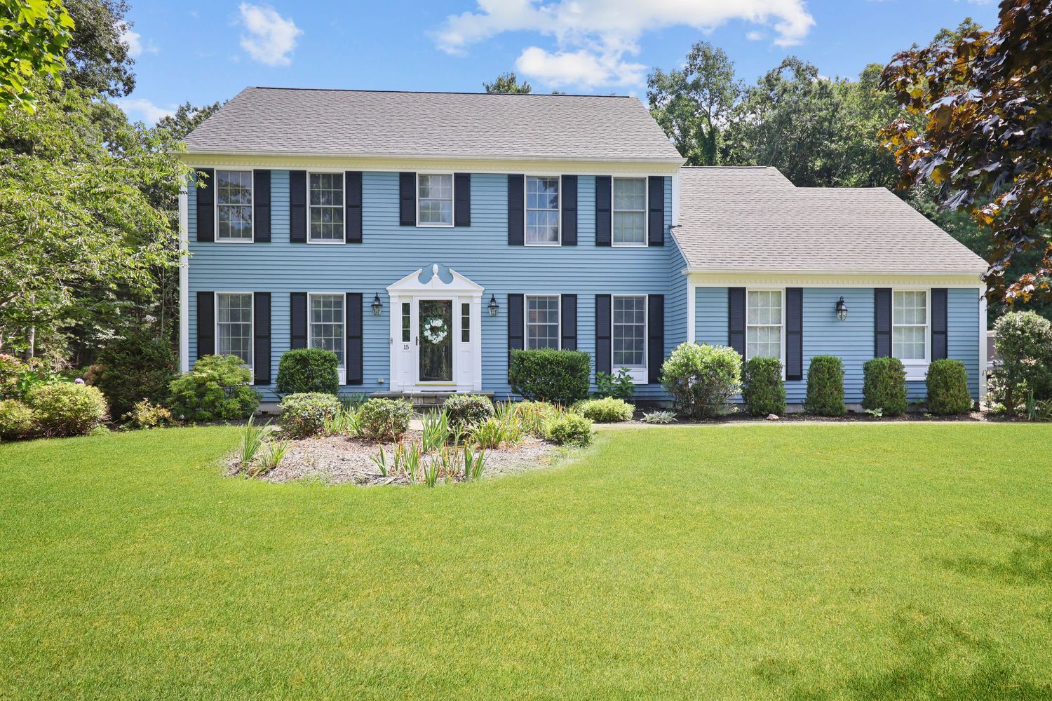 Traditional blue colonial style house with white trim and manicured lawn on sunny day.