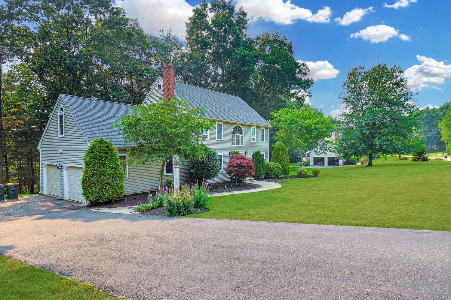 Colonial style house with attached garage on landscaped property under blue sky.