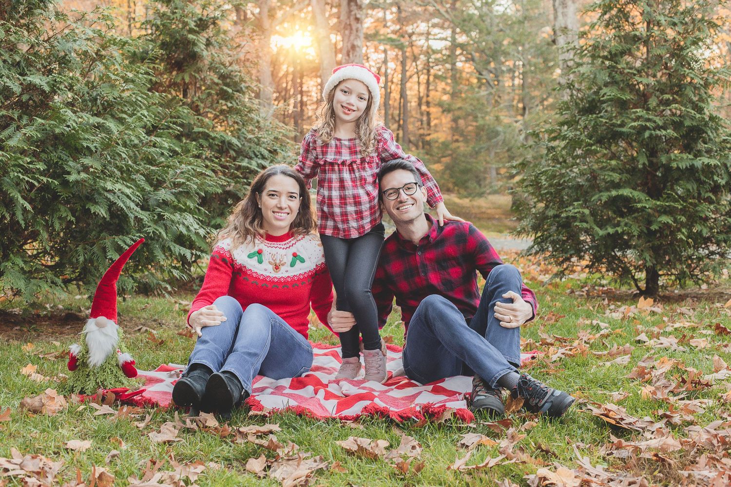 Family sitting on red blanket for holiday photo session in evergreen forest.