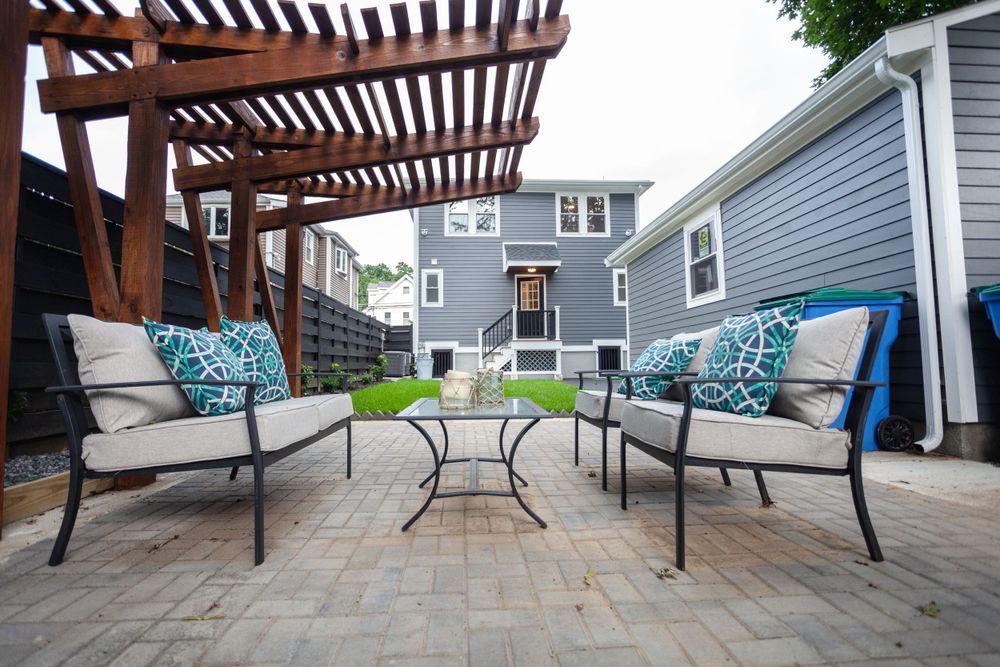 Modern backyard patio with lounge chairs, a pergola, and a gray house in the background.
