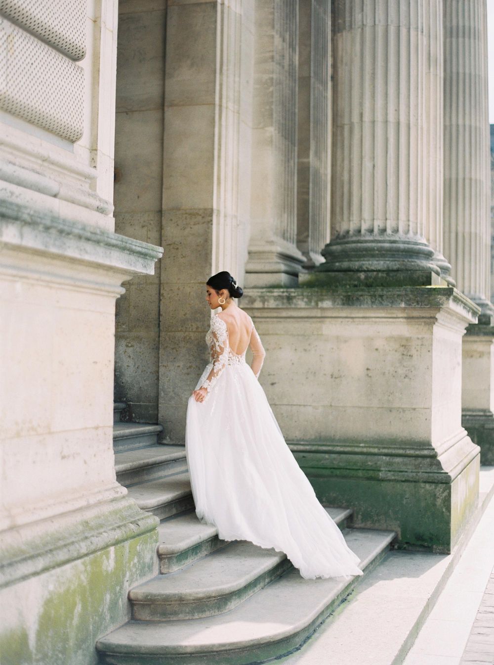 A bride in a beautiful wedding dress gracefully descending steps at the luxurious Louvre in Paris.