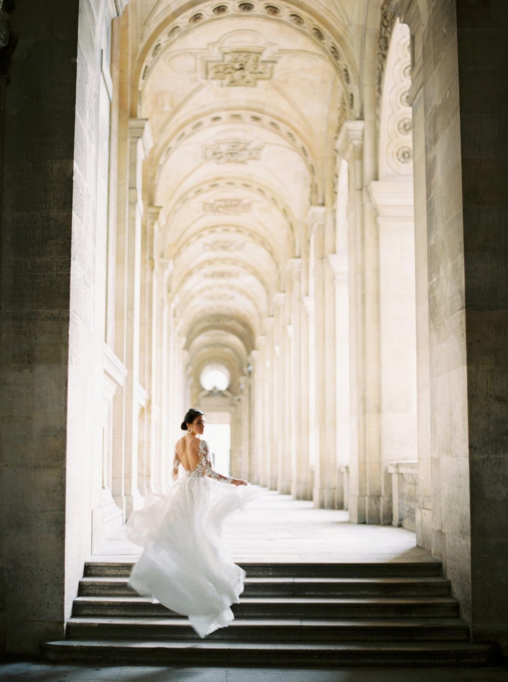 A beautiful bride in an elegant white dress gracefully descending the stairs at the luxurious Louvre in Paris.