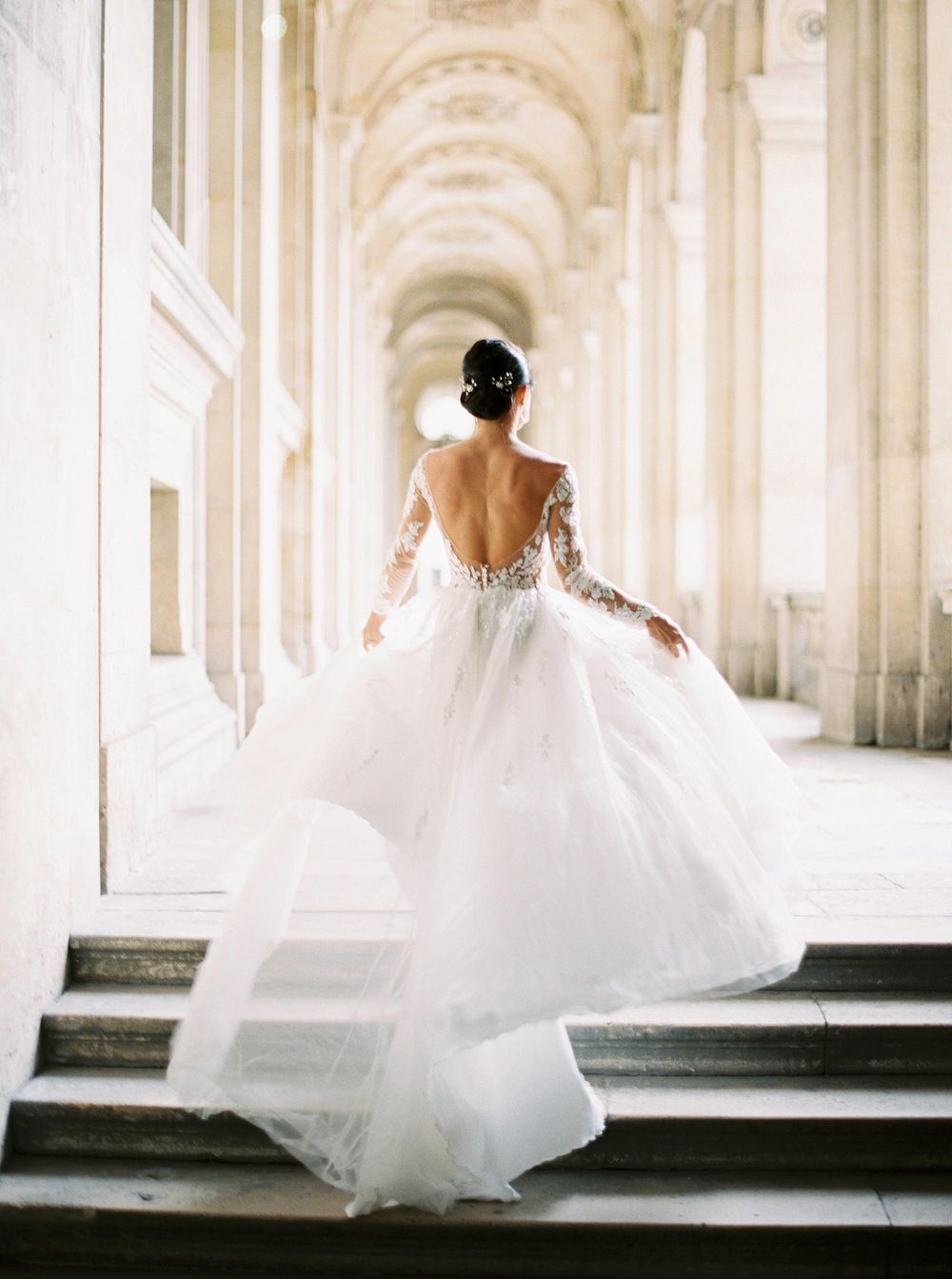 An exquisite bride in a white dress energetically descending the stairs at the lavish Louvre in Paris.