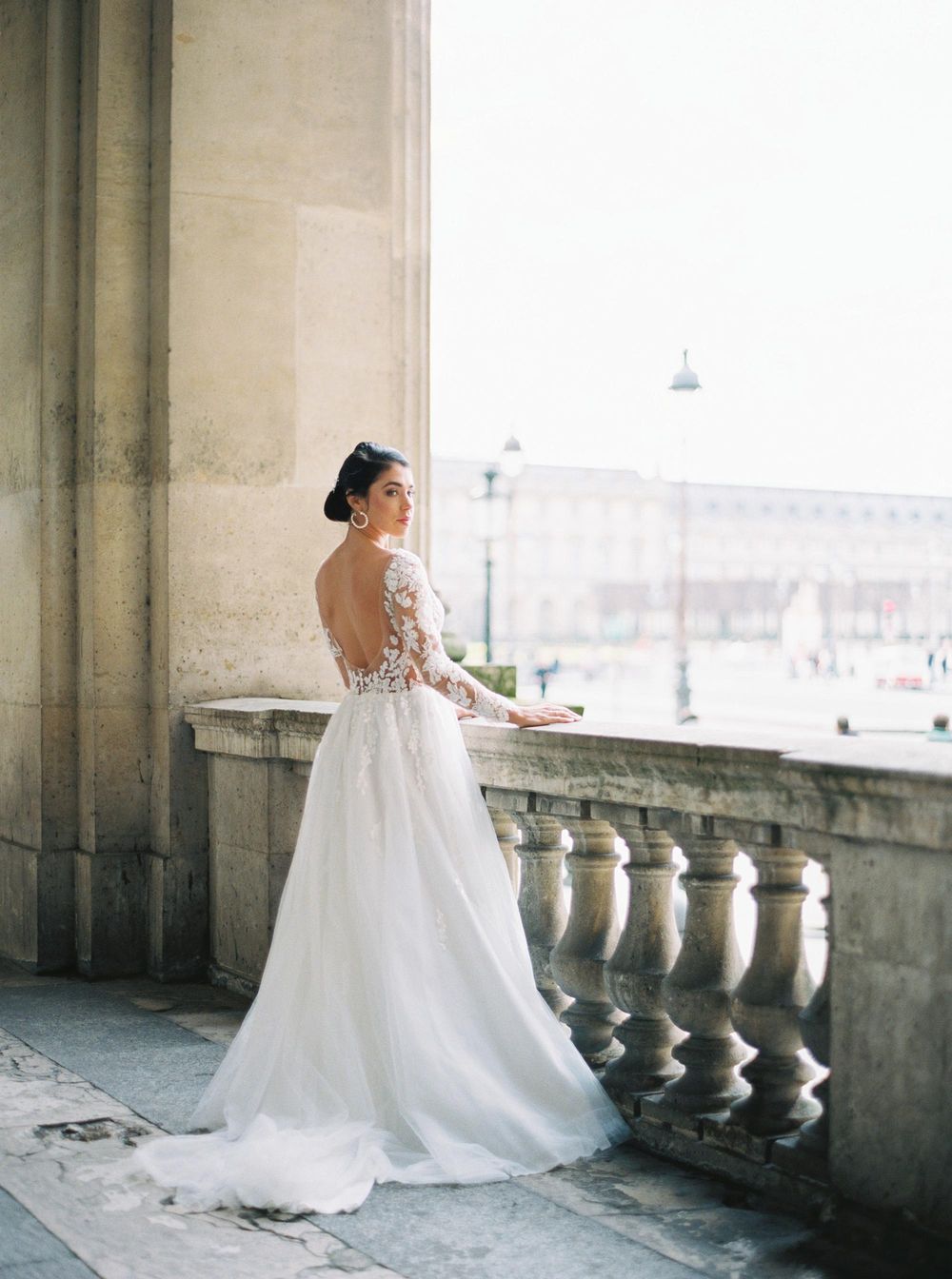 A luxury bride in a wedding dress standing on a balcony at Louvre, Paris.