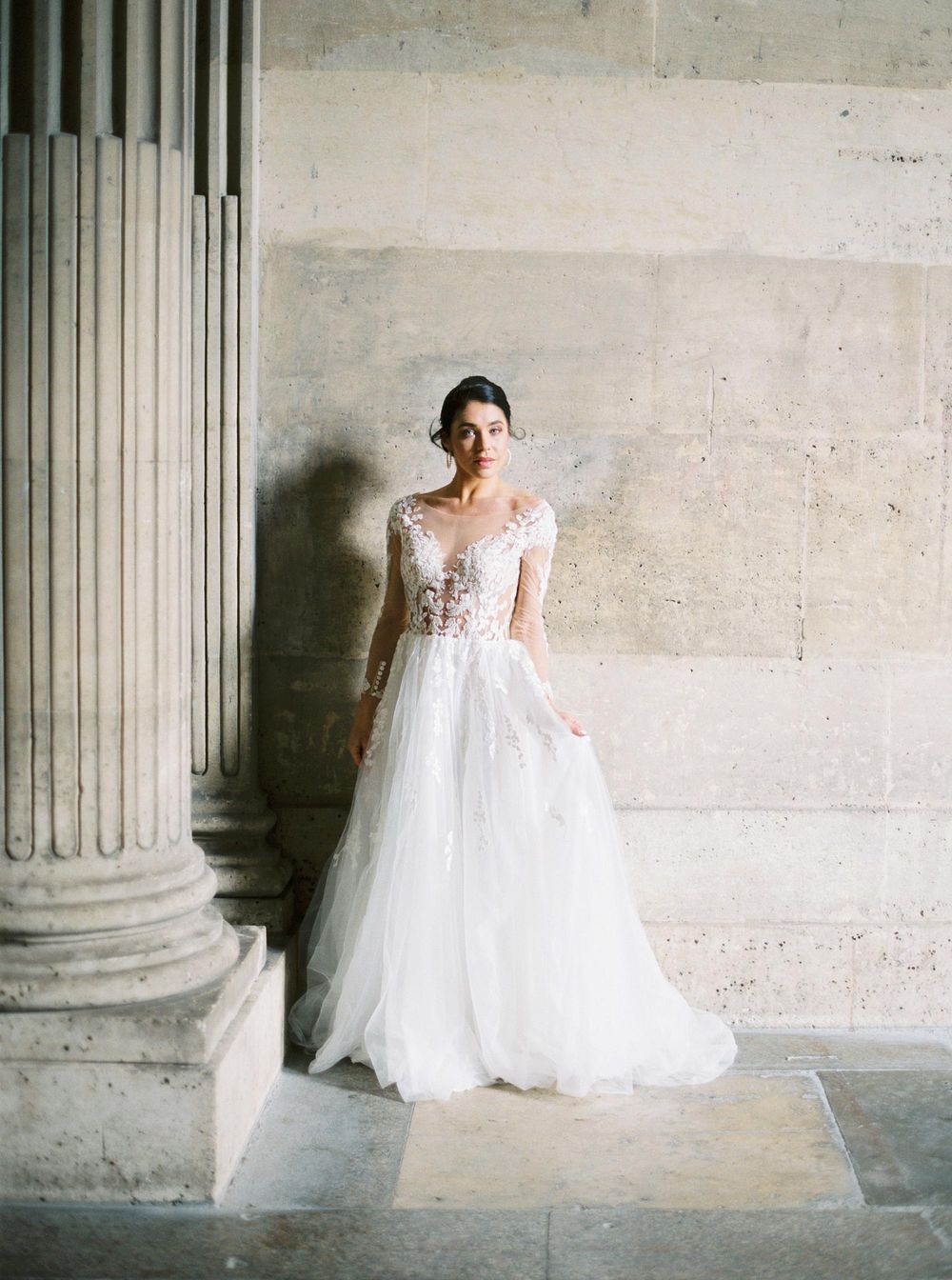 Elegant bride in wedding attire posing by columns at Louvre, Paris.