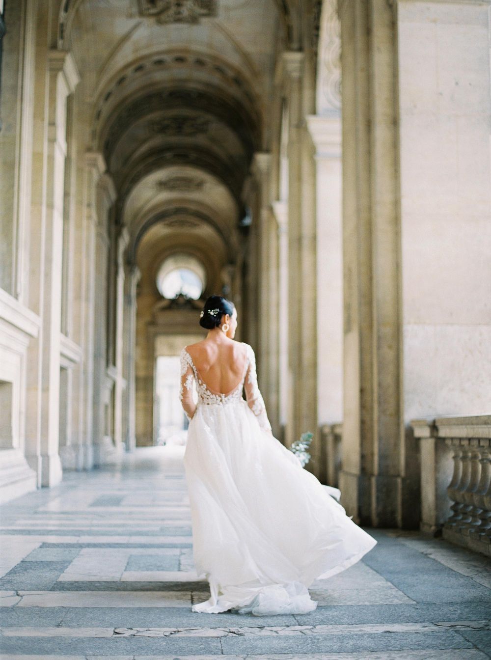 A stunning bride in a white dress running with excitement at the opulent Louvre in Paris.