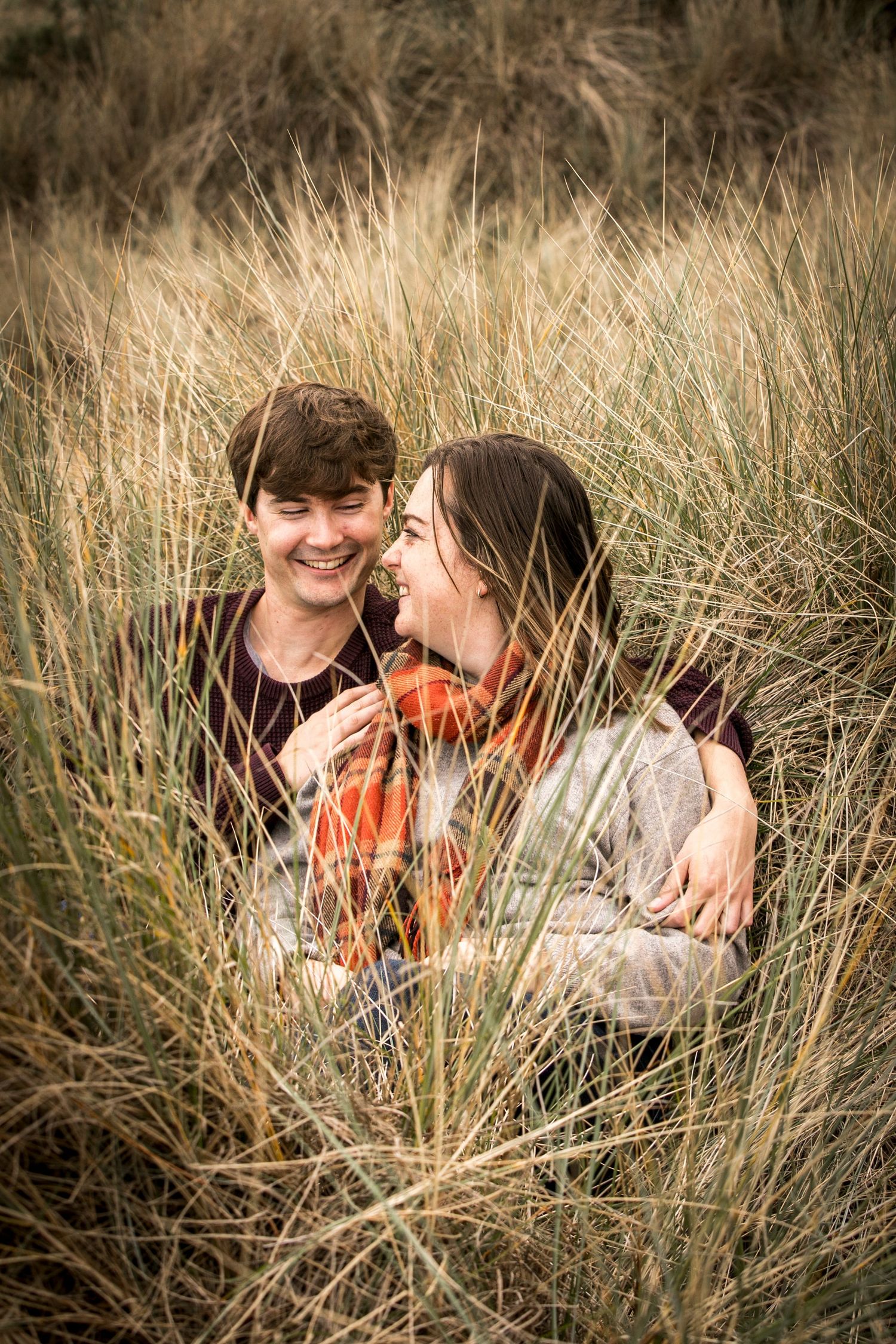 Intimate couple nestled in tall beach grass during golden hour.