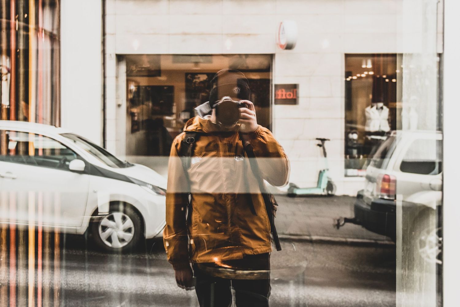 A person in a brown jacket stands in front of a window display at a shop.