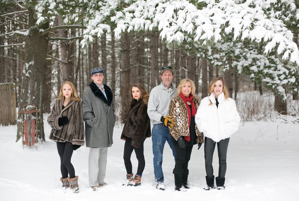 Family of six posing together in snowy winter forest wearing stylish coats.