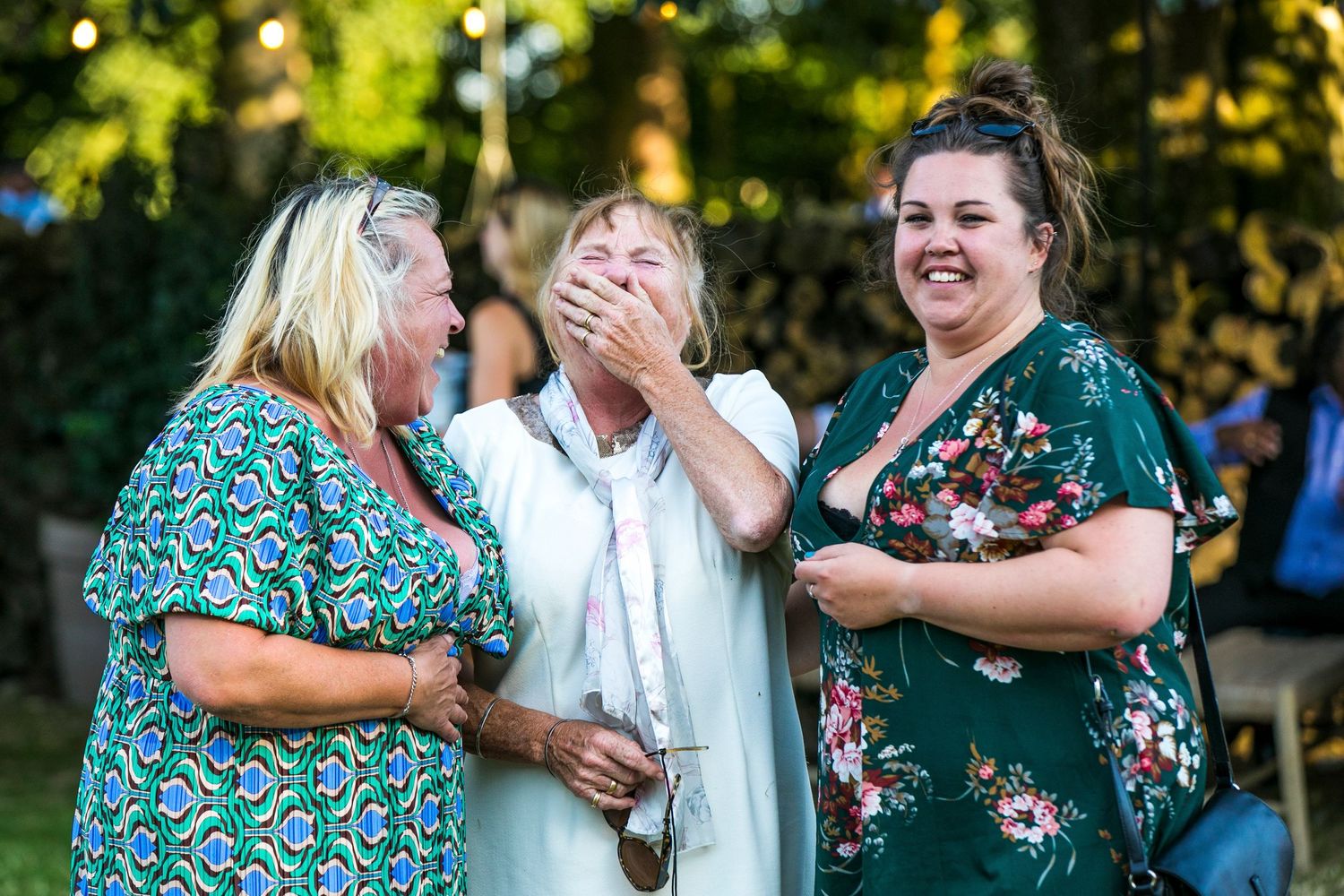 Wedding guests laughing and embracing during outdoor summer celebration.