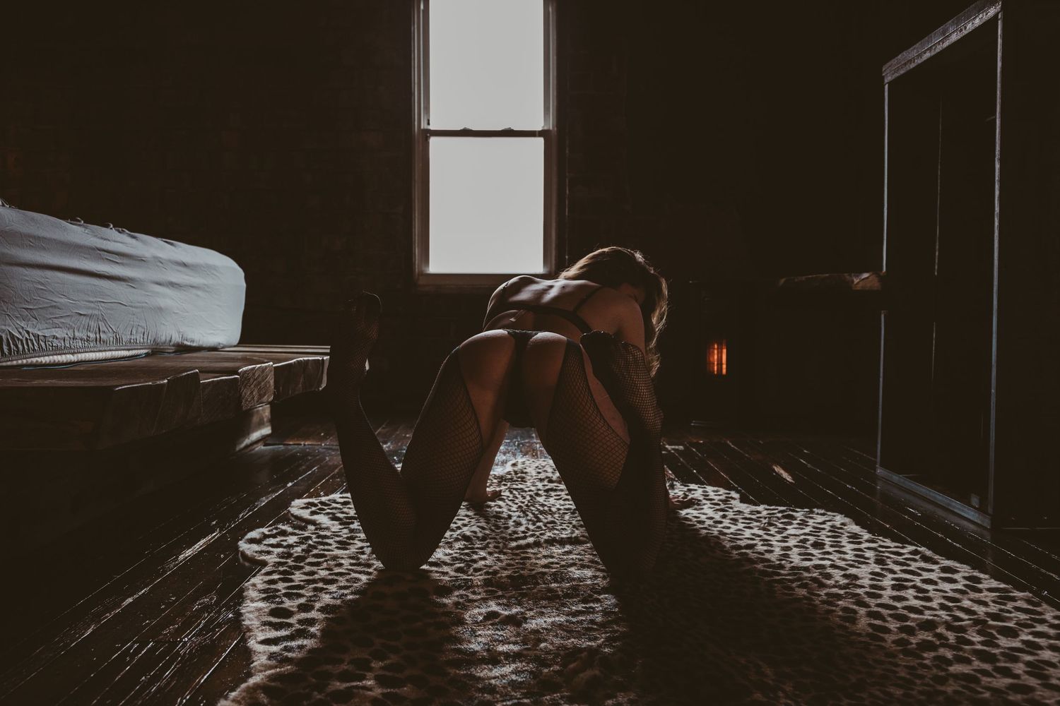 A dark interior bedroom scene with empty chairs and tables illuminated by soft natural light streaming through windows.